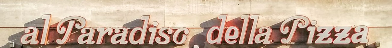 L'insegna «al Paradiso della Pizza», lettere in corsivo rosso sul travertino della facciata
