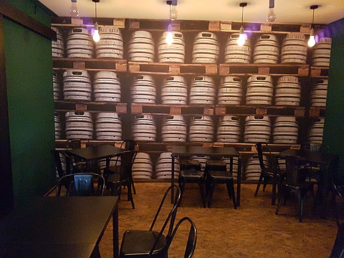 La sala di All Beer col muro di fusti di birra