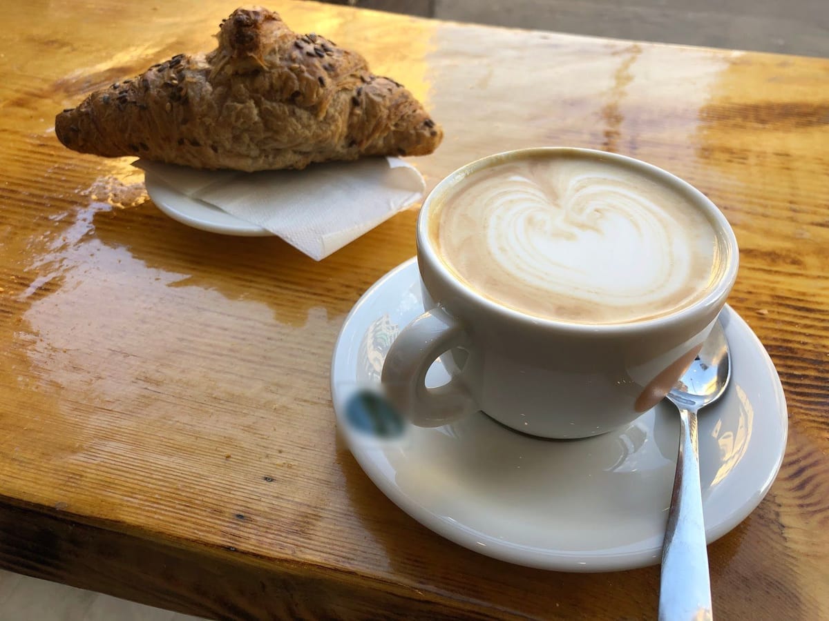 Il cappuccino col cuore di latte e una brioche coi semi sulla mensola di legno.