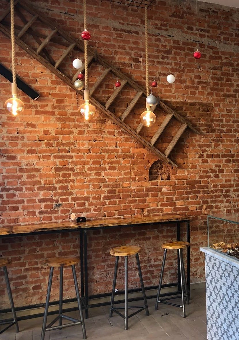 Il muro di mattoni con la scala di legno di sbieco, le lampadine sulle corde di juta, un piccolo arco nel mattone e la mensola con gli sgabelli.