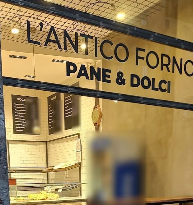 La vetrina di sera, accesa: «L'Antico Forno, Pane & Dolci», le lavagne, la mensola con gli sgabelli.