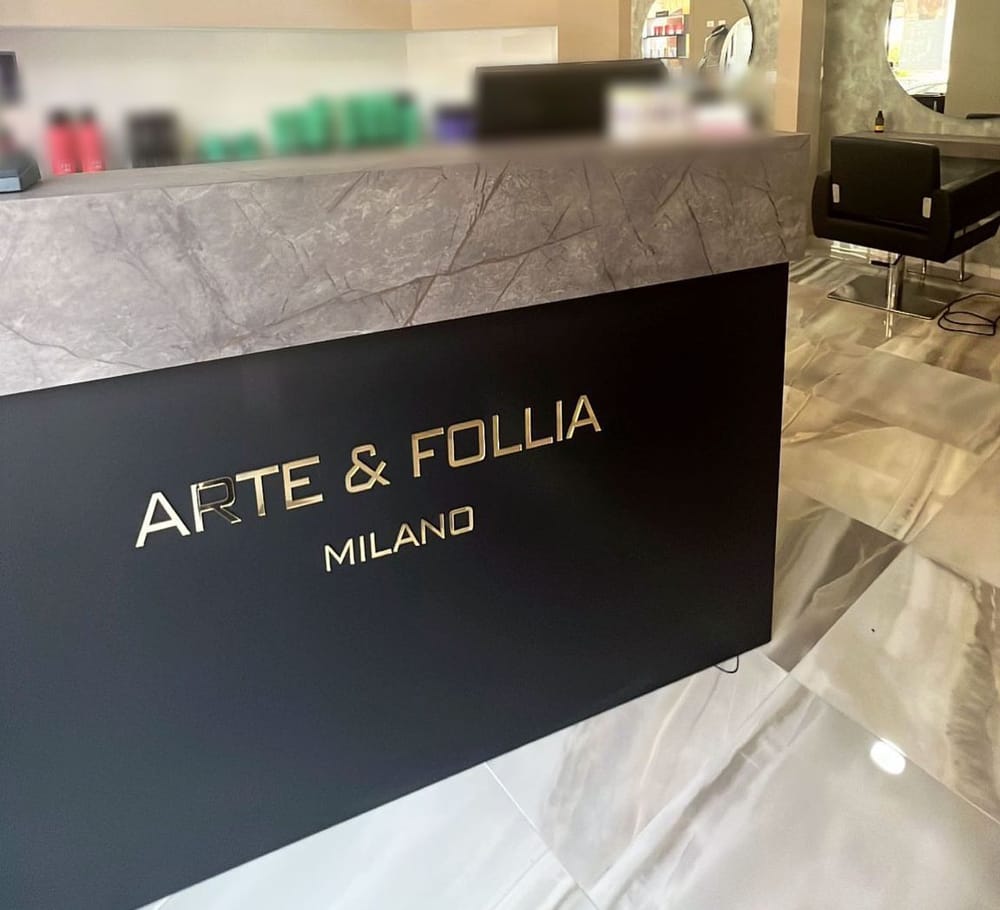 Il banco all'ingresso: nero, con le lettere dorate ARTE & FOLLIA MILANO, il piano di marmo grigio e dietro gli scaffali