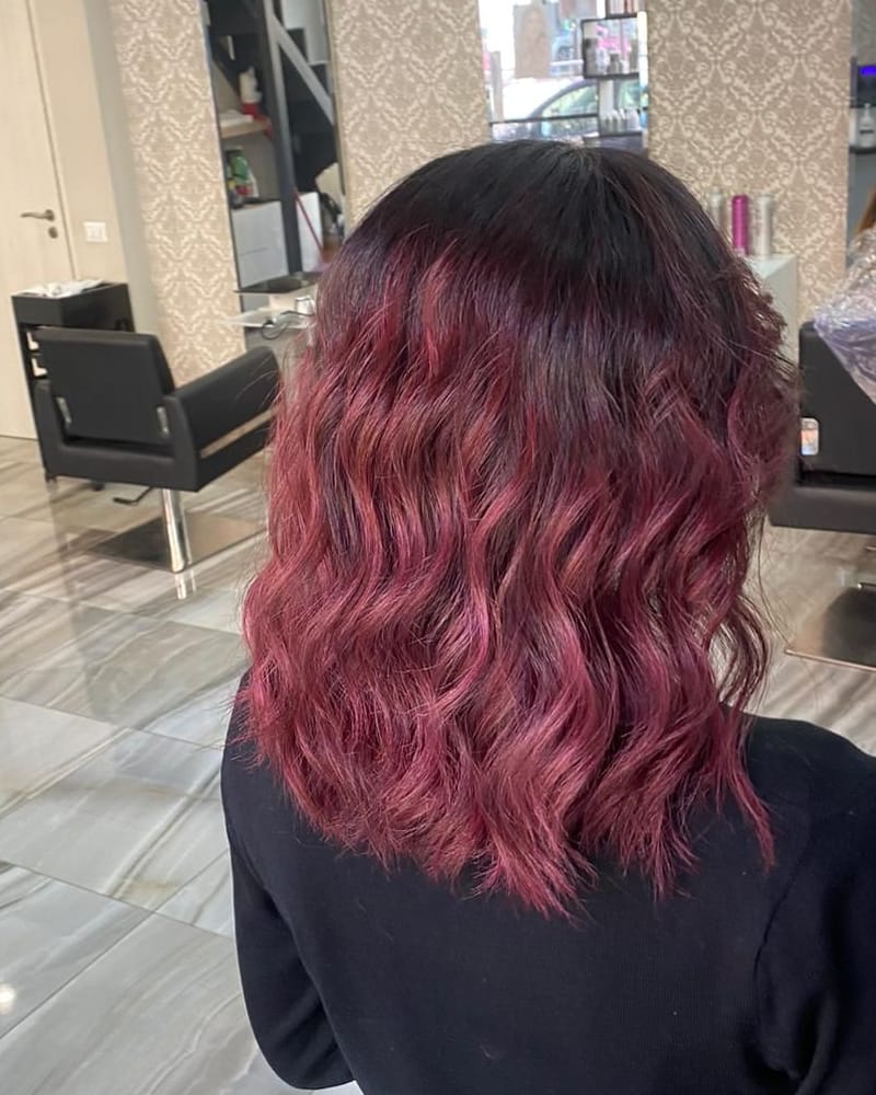 Capelli mossi color borgogna, con la radice scura, di spalle, nel salone