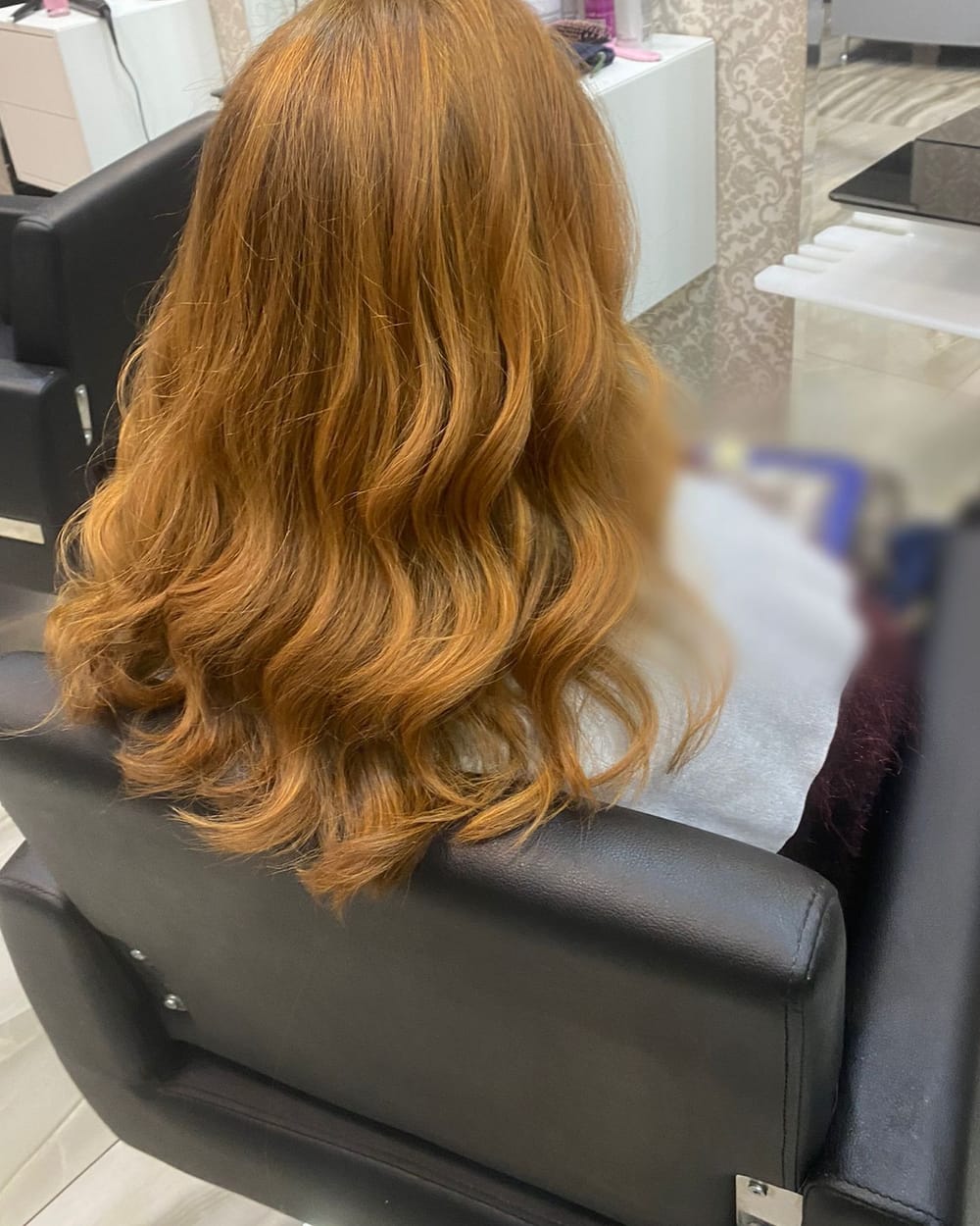 Capelli ramati e mossi, di spalle, su una poltrona nera del salone