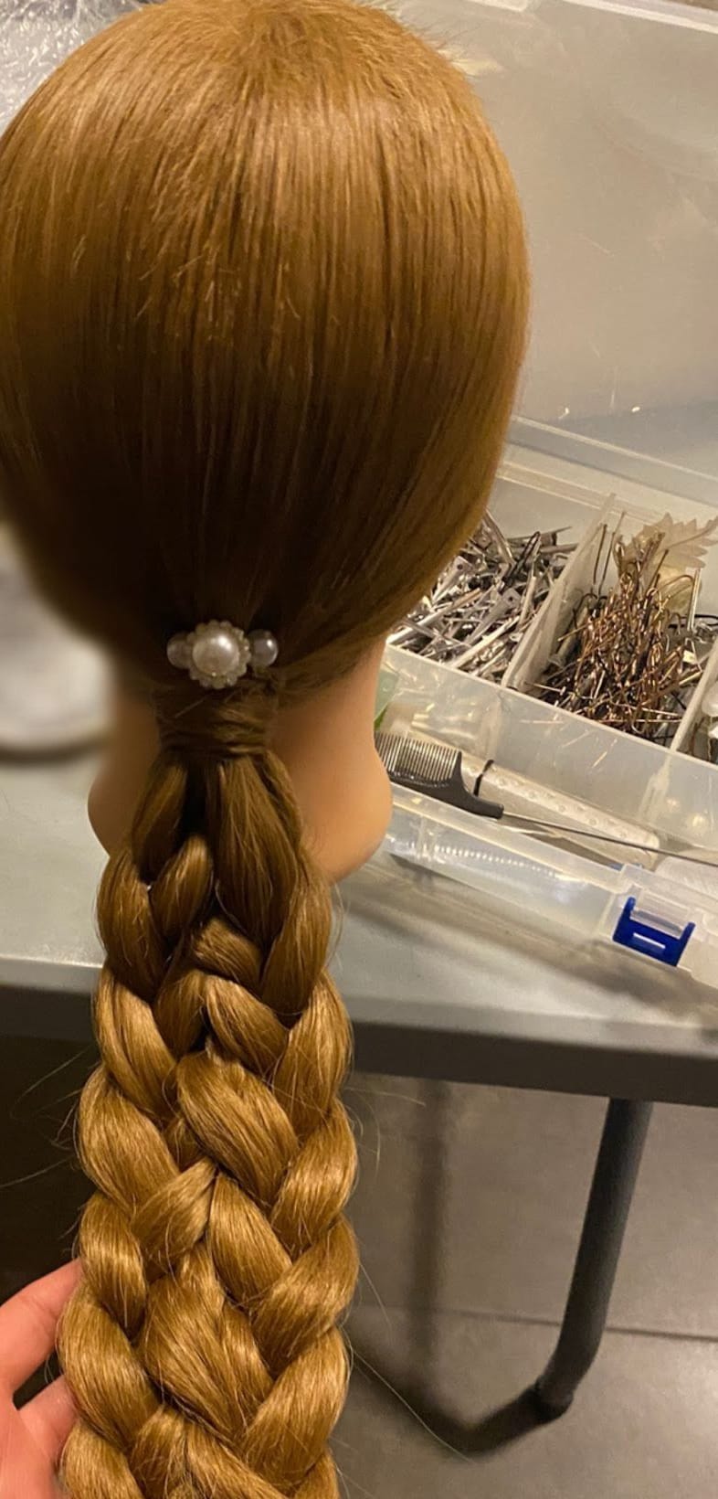 Una lunga treccia su una testa da esercitazione, fermata con un fermaglio di perle, sul bancone di lavoro