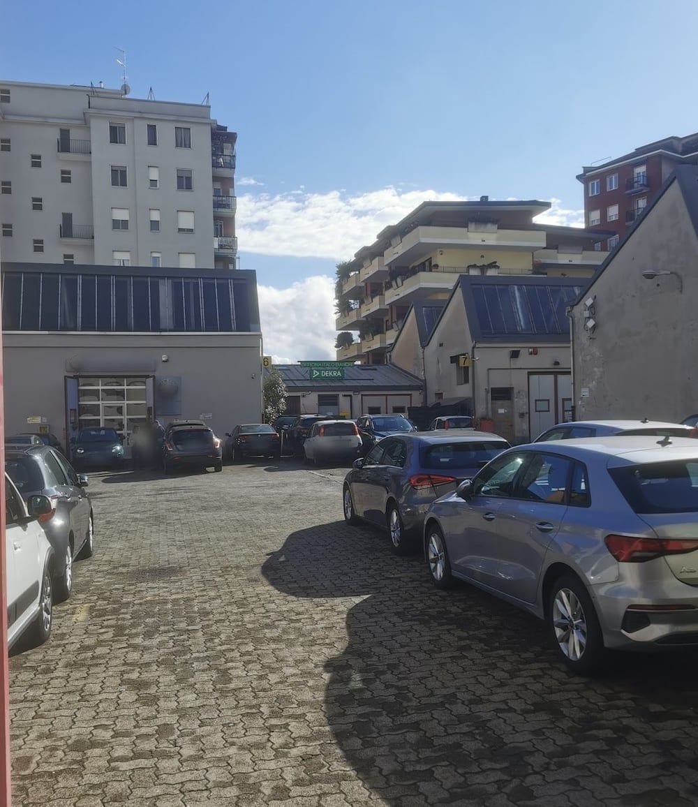 Il cortile dell'officina con le auto in fila e l'insegna verde DEKRA in fondo