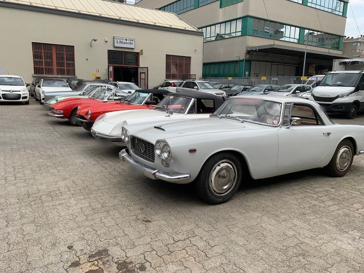 Una fila di auto d'epoca nel cortile: una coupé bianca e due spider rosse davanti all'officina