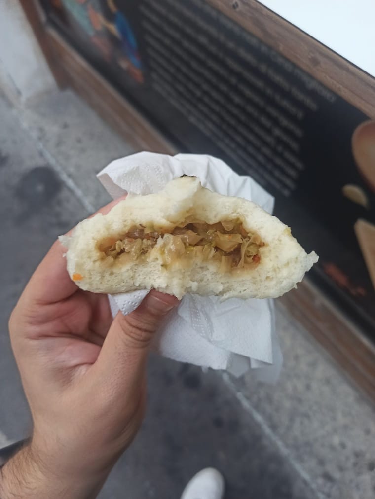 Un bao aperto a metà, col ripieno, tenuto nella carta.