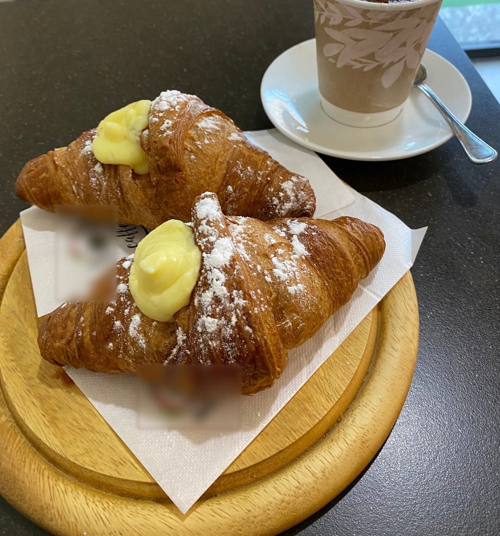 Due cornetti alla crema sul tagliere tondo e un cappuccino.