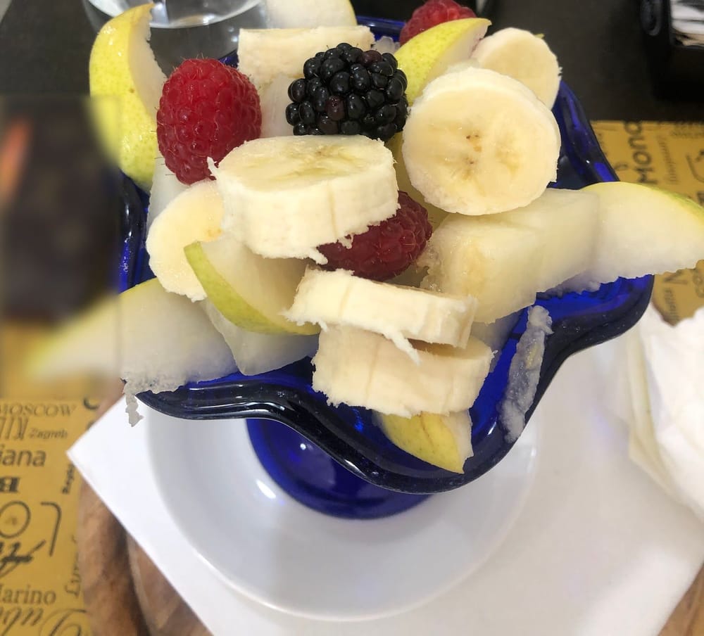 La coppa di vetro blu con la banana, la pera, i lamponi e la mora.
