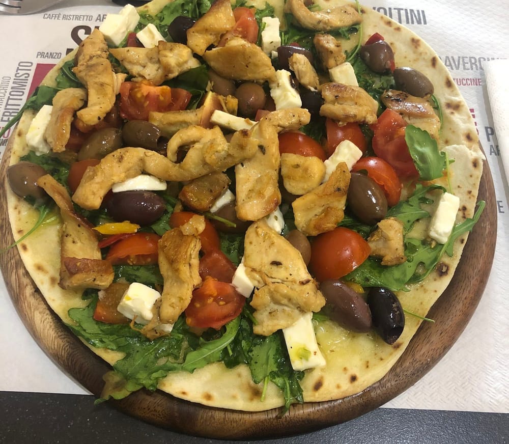 Una piadina col pollo, la rucola, le olive, i pomodorini e la feta, sul tagliere tondo.