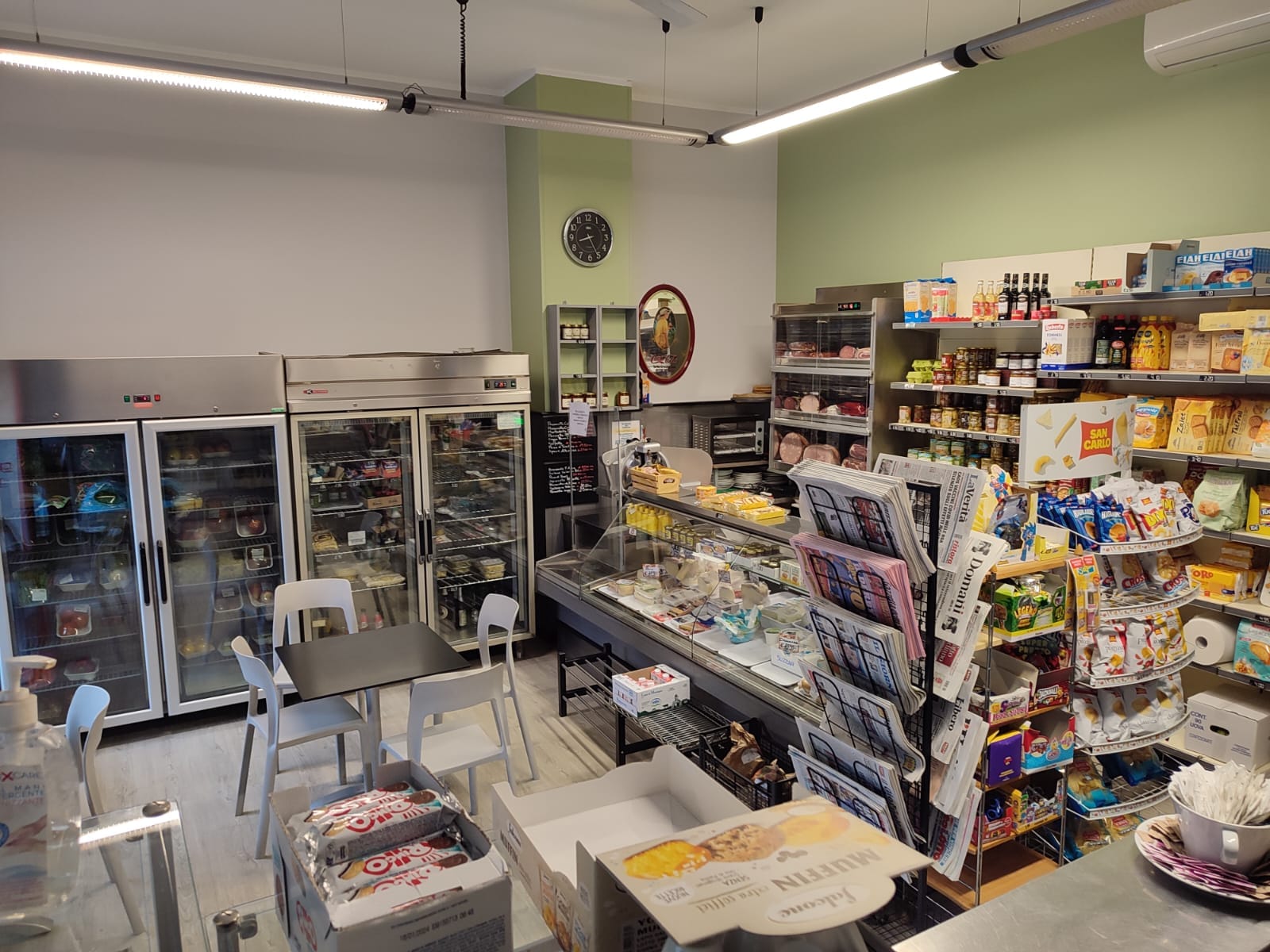 Il banco del bar con i frigoriferi, la rastrelliera dei quotidiani e le pareti verde salvia