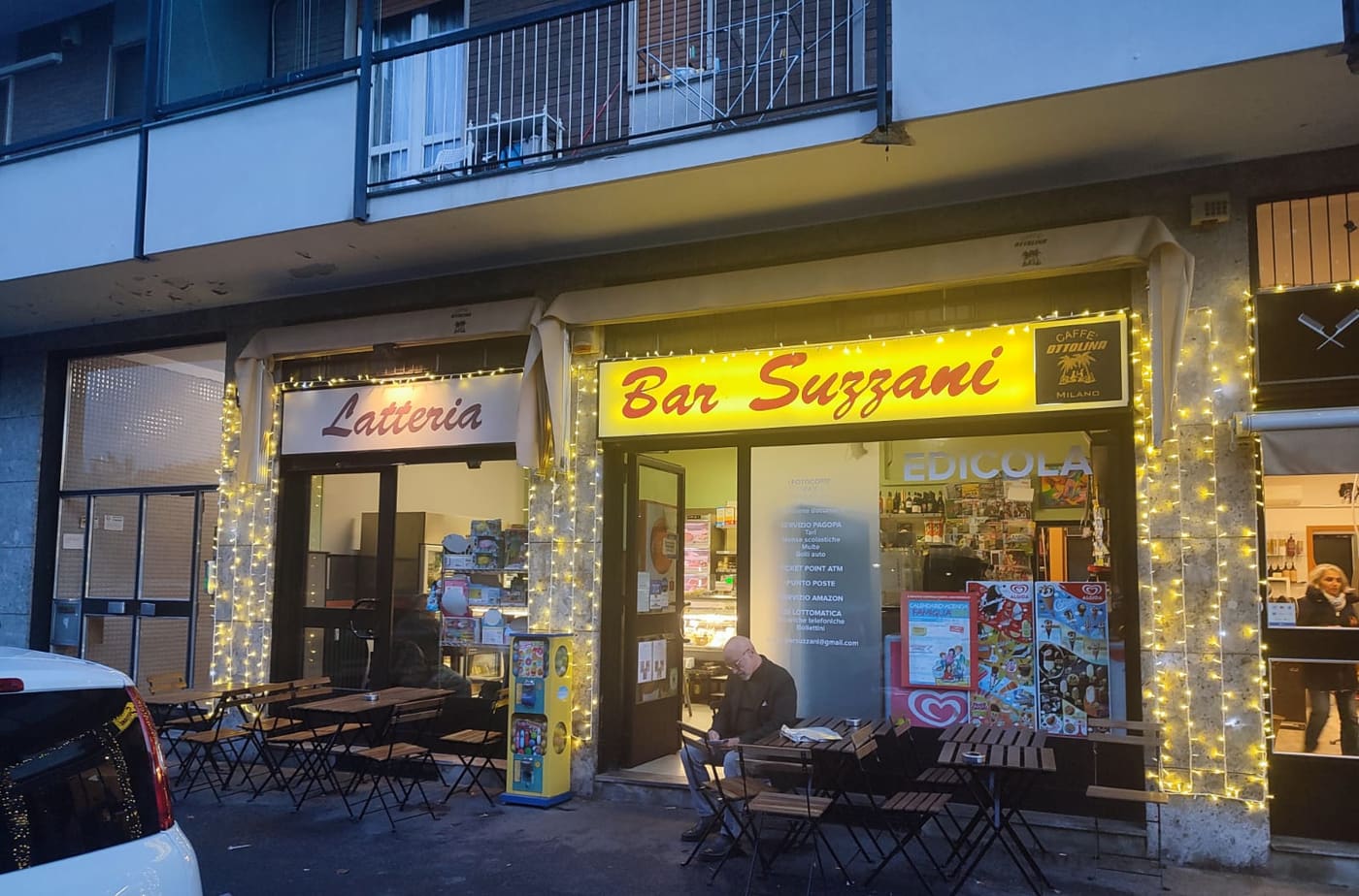 La facciata del bar di sera, con le luci e l'insegna gialla Bar Suzzani accesa