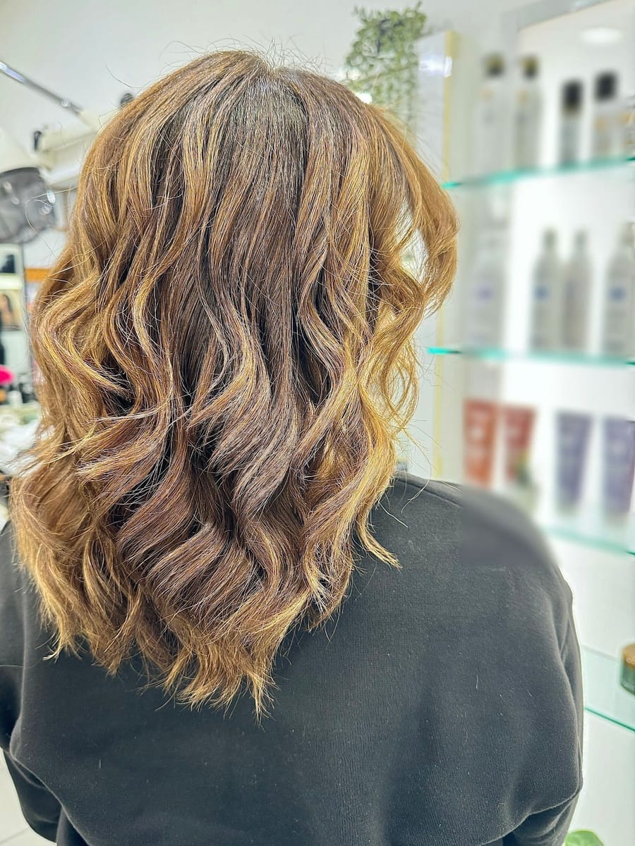 Capelli mossi color miele, di spalle, accanto alle mensole di vetro del salone.