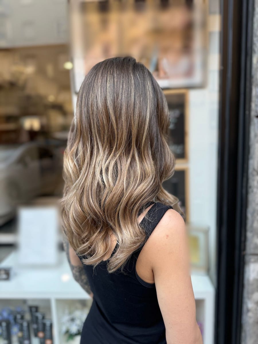 Capelli lunghi con le schiariture, di spalle, alla vetrina del salone.