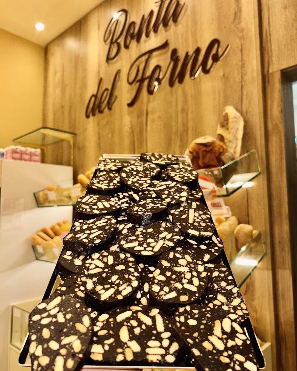 La parete di legno con il logo «Bontà del Forno» in corsivo dorato e, davanti, un vassoio di torrone al cioccolato con mandorle