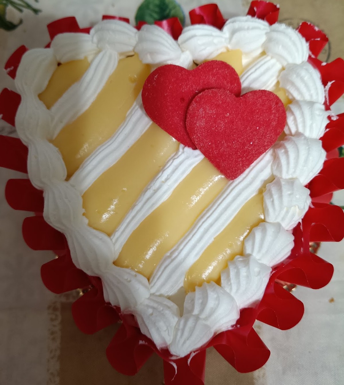 Una torta a forma di cuore con crema, panna montata e due cuori di pasta rossa al centro
