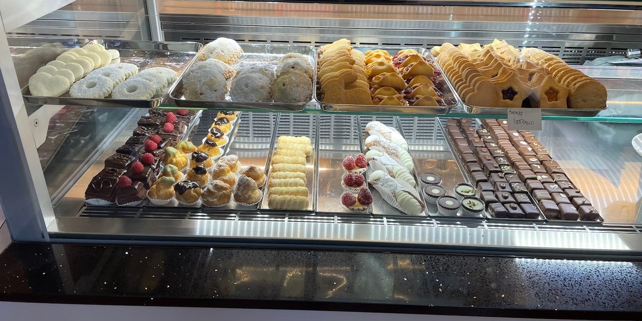Il banco dei dolci: pasticcini, bignè, tartellette alla frutta e cioccolatini su due ripiani.