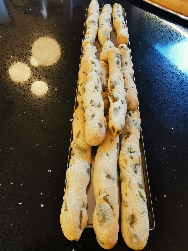 Bastoncini di pane alle olive, lunghi e dorati, sul vassoio.
