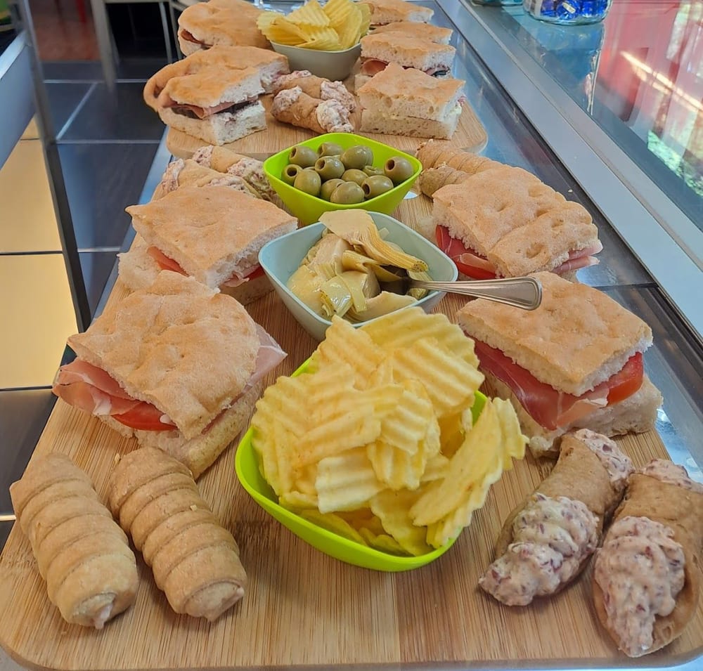 Un buffet sul banco: focaccine farcite, tramezzini, patatine, olive, cannoncini salati.