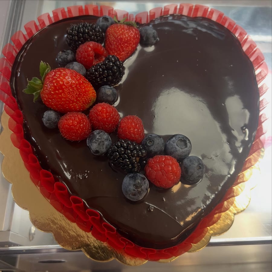 Una torta a cuore glassata al cioccolato, con fragole, lamponi, more e mirtilli, la gala rossa e il disco dorato.