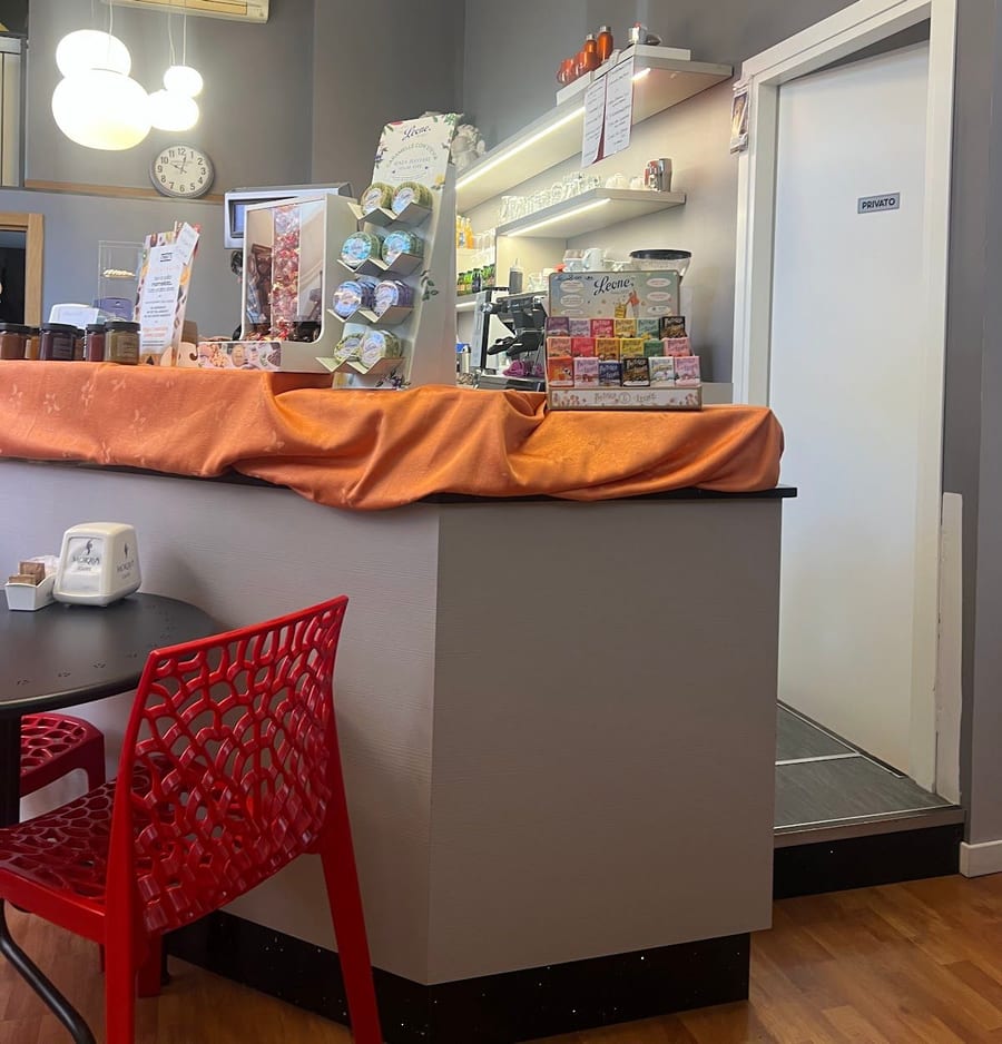 L'interno: il bancone con la tovaglia arancio e una sedia rossa traforata.