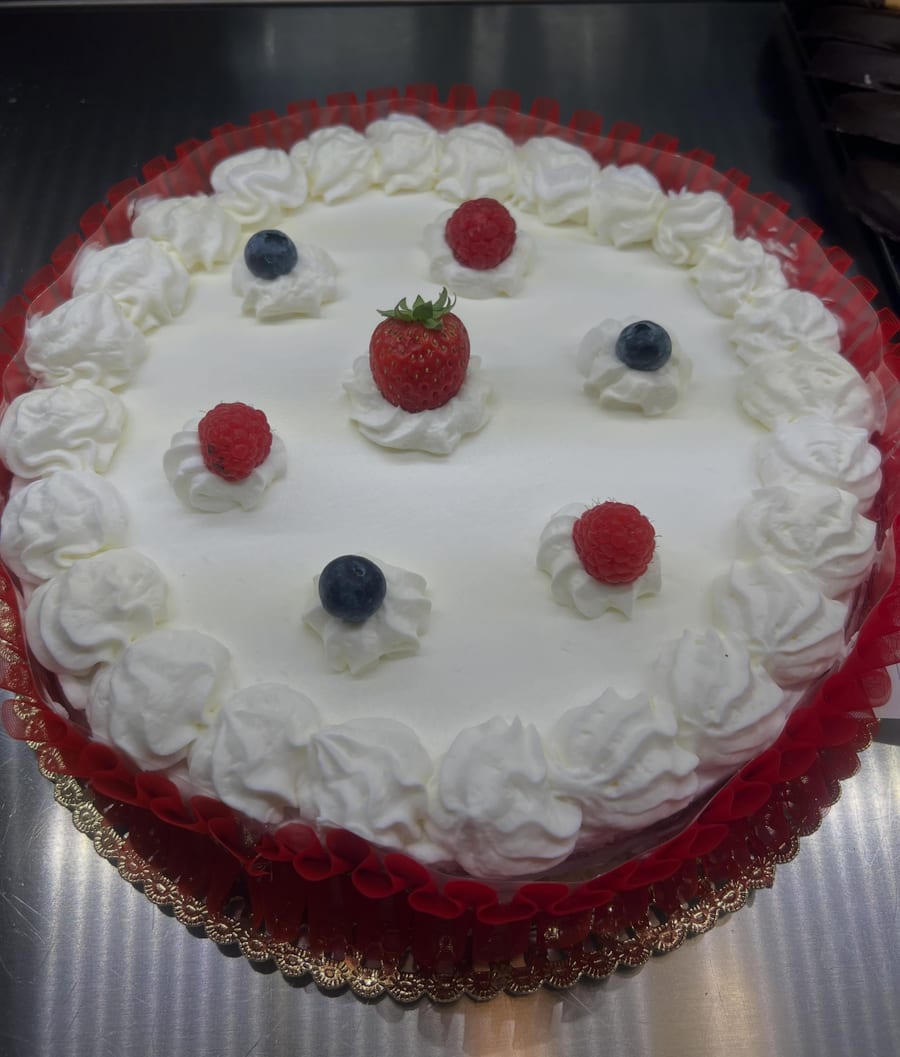 Una torta alla panna coi ciuffi, una fragola, lamponi e mirtilli, la gala rossa.