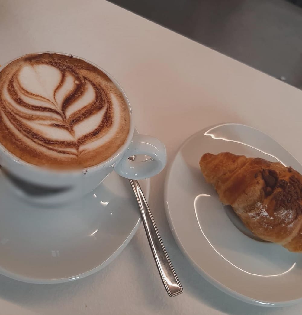 Il cappuccino con la rosetta e il cornetto sul piattino.