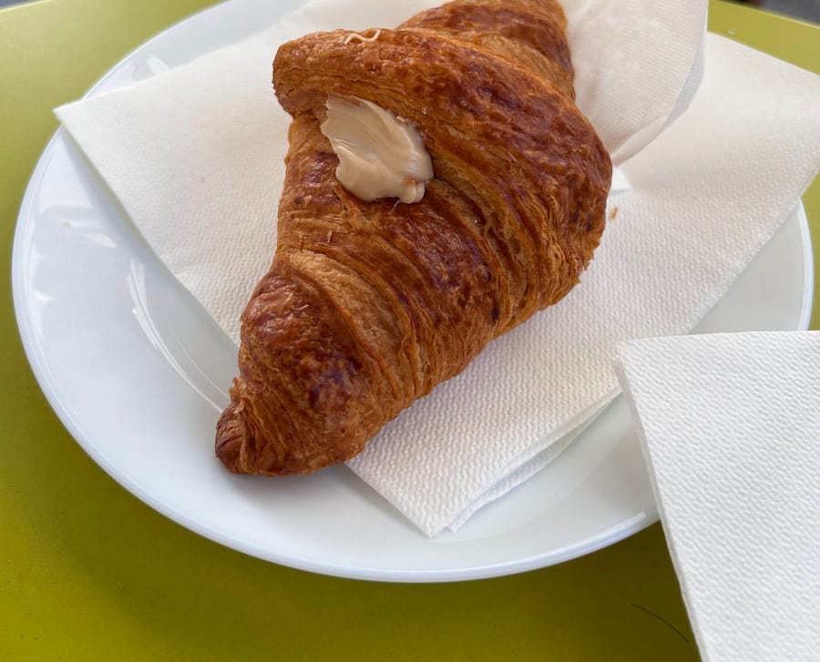Un cornetto alla crema sul piatto col tovagliolo, sul tavolino verde.