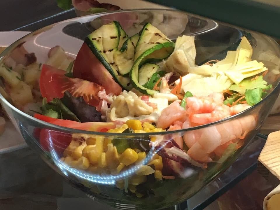Un'insalatona in coppa con gamberi, zucchine grigliate, mais e carciofi.