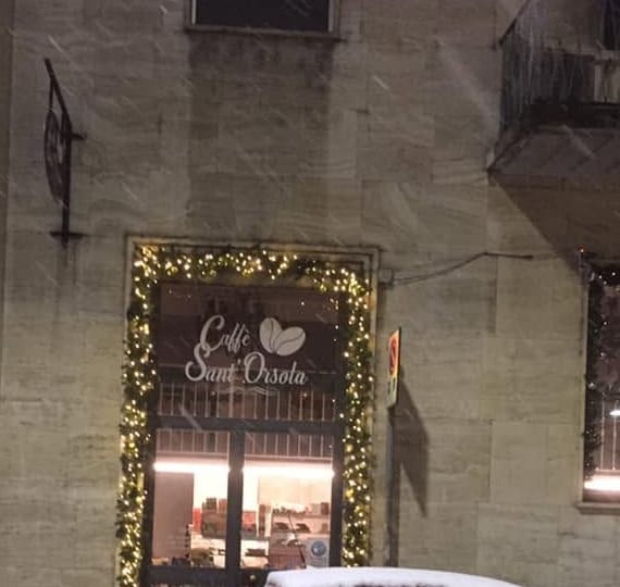 La facciata di notte sotto la neve, la vetrina accesa con la ghirlanda.