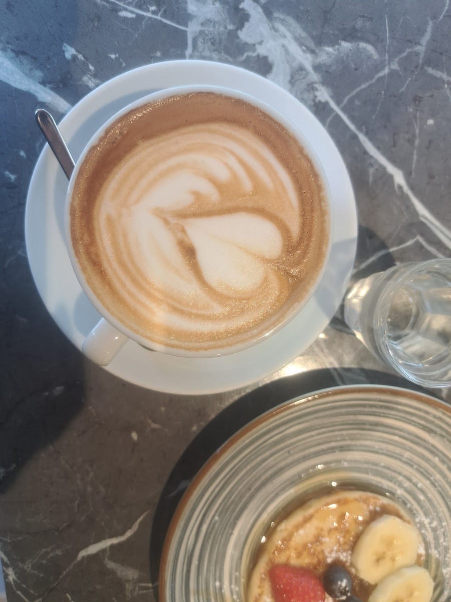 Dall'alto: un cappuccino col cuore e una ciotola di pancake con banana, fragola e mirtilli sul tavolo di marmo nero