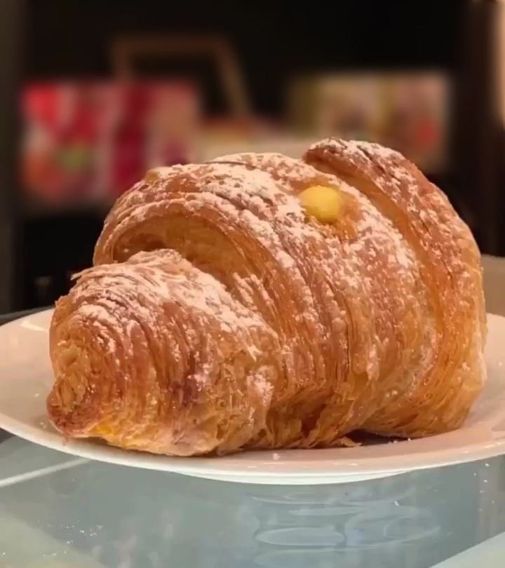 Un cornetto sfogliato con lo zucchero a velo e la crema che spunta in cima, su un piatto bianco