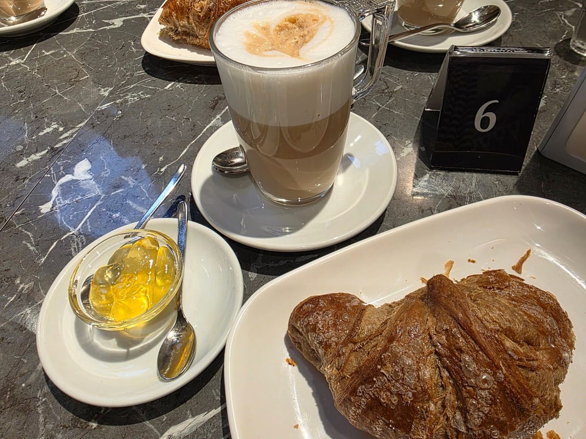 Un latte macchiato nel bicchiere, un cornetto e una ciotolina di miele sul tavolo di marmo nero col numero 6