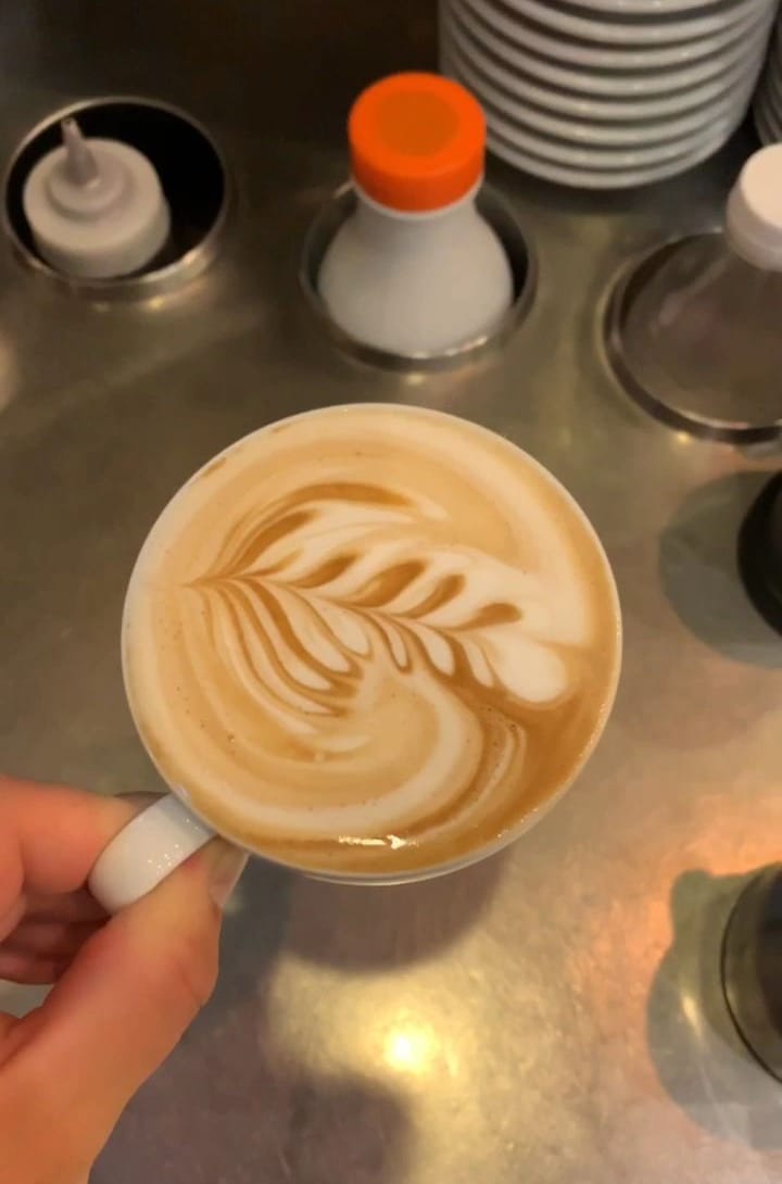 Un cappuccino con la rosetta disegnata nella schiuma, tenuto per il manico sopra il banco