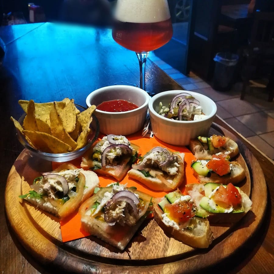 Un tagliere di bruschette con i nachos, due ciotoline di salsa e un calice di birra ambrata