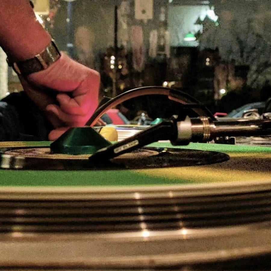 La mano di un DJ sul braccio di un giradischi, di sera