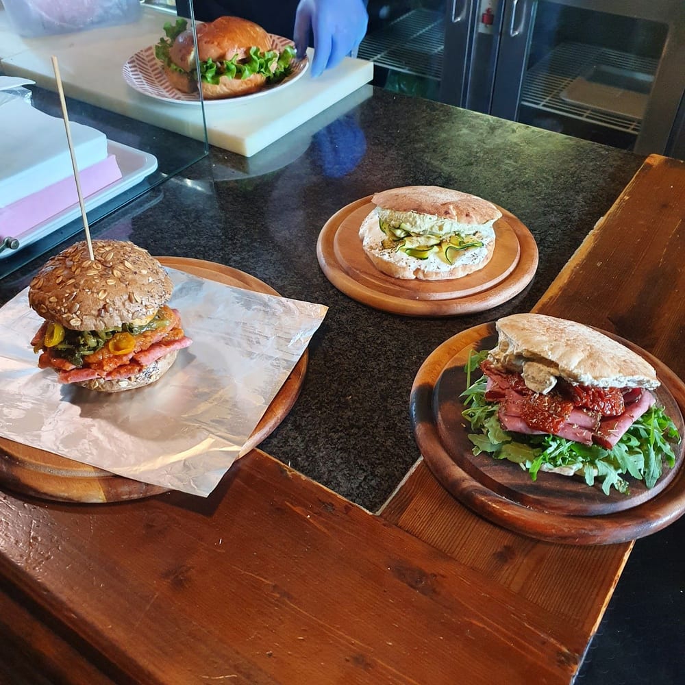 Tre panini sui taglieri di legno sul bancone: uno coi semi, uno con le zucchine, uno con la carne e la rucola