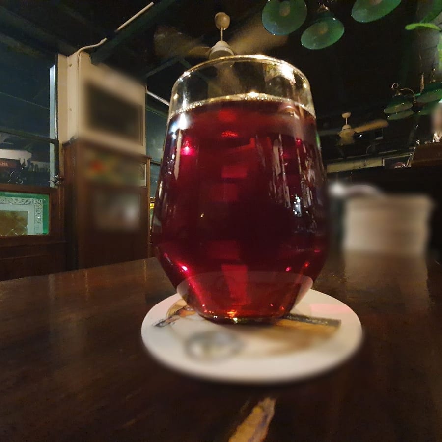 Un bicchiere di birra rosso scuro sul bancone, con le lampade verdi in alto