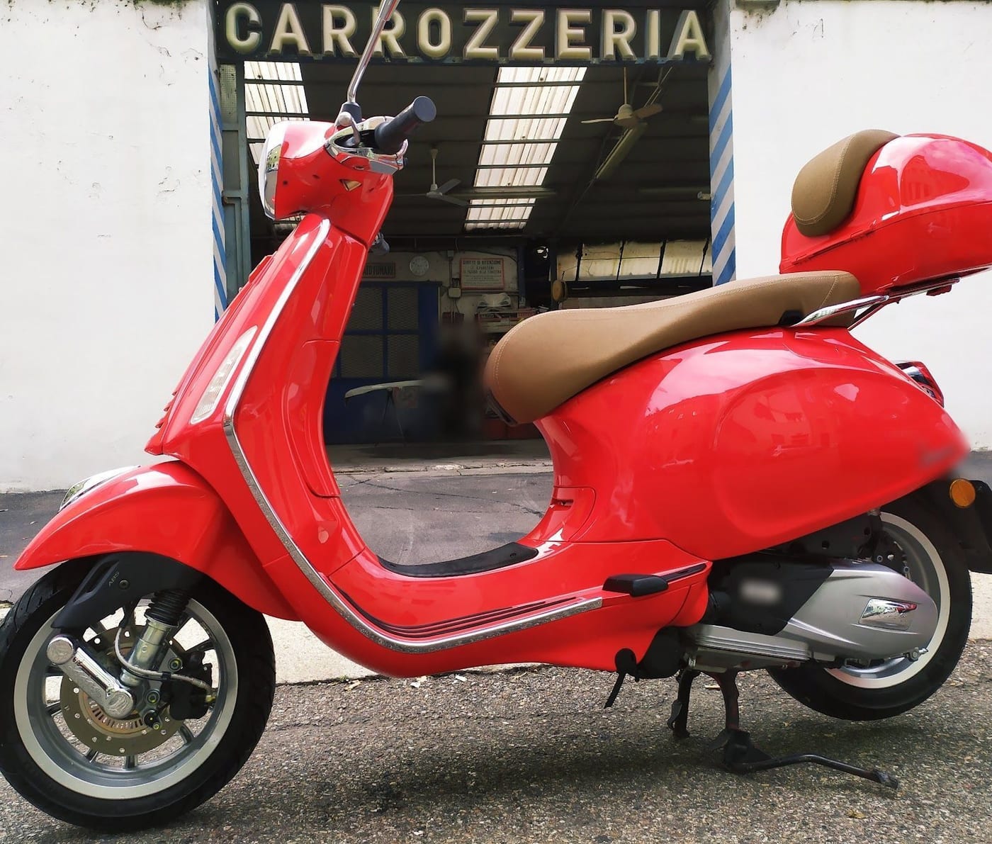 Una Vespa rossa davanti all'ingresso dell'officina, sotto la grande insegna CARROZZERIA