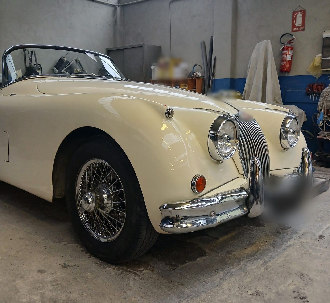Una Jaguar XK color crema coi cerchi a raggi, in officina