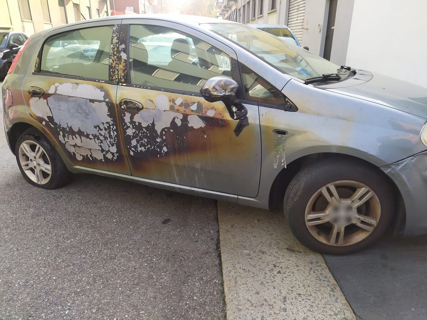 La fiancata di una Fiat Grande Punto grigia, con la vernice rovinata e bruciata e lo specchietto fuso