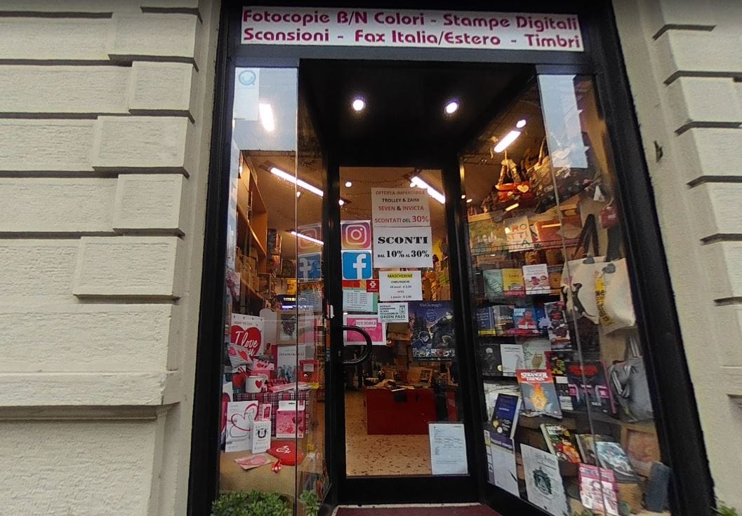 L'ingresso della cartolibreria con la vetrina piena e gli adesivi dei social sulla porta