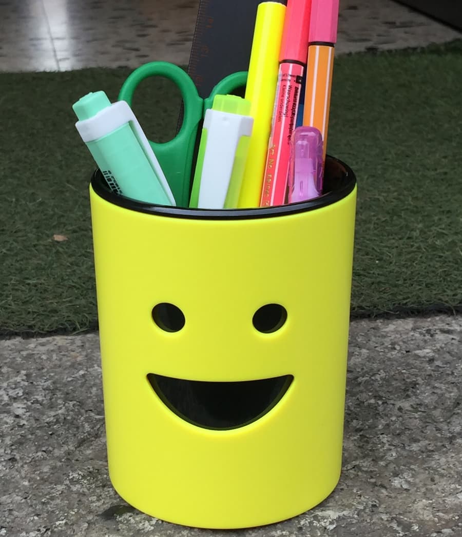 Un portapenne giallo con la faccia sorridente, pieno di pennarelli