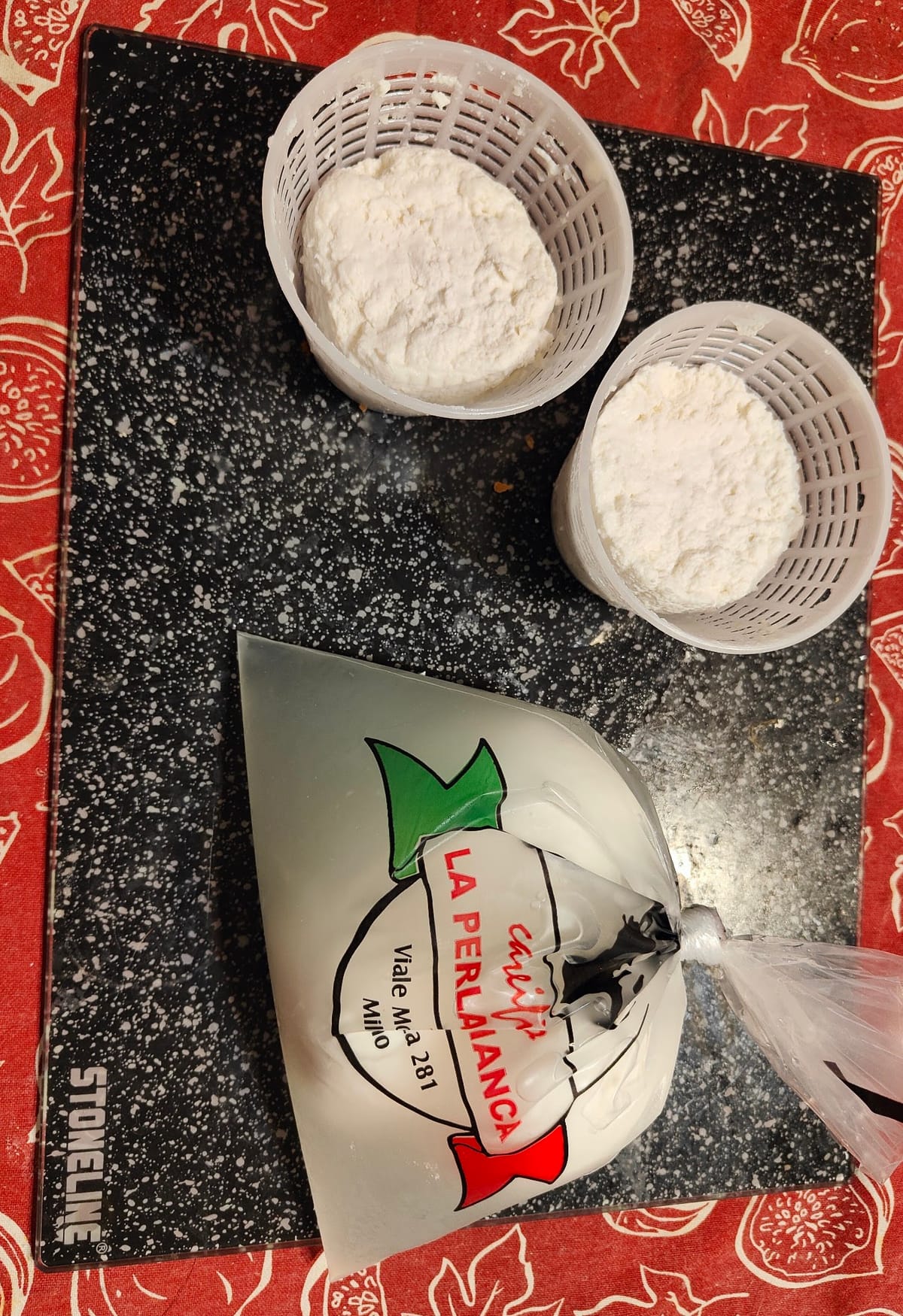 Due ricotte nelle fuscelle e la busta della mozzarella con il logo La Perla Bianca