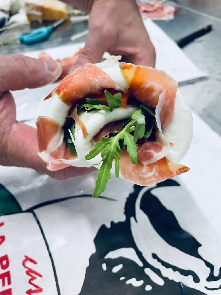 Una mano tiene un involtino di mozzarella con prosciutto crudo e rucola