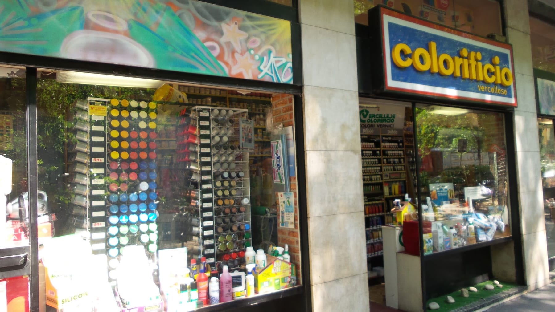 La vetrina del Colorificio Vercellese: insegna colorata, murale e colonne di bombolette spray