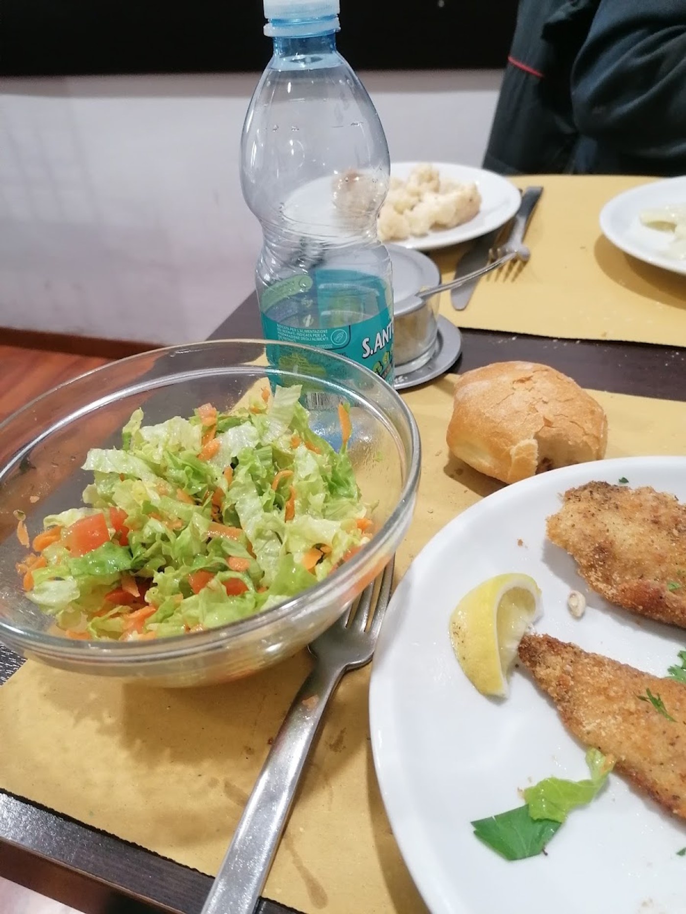Un pranzo servito: insalata mista in una ciotola di vetro, una cotoletta impanata con il limone, il pane e l'acqua