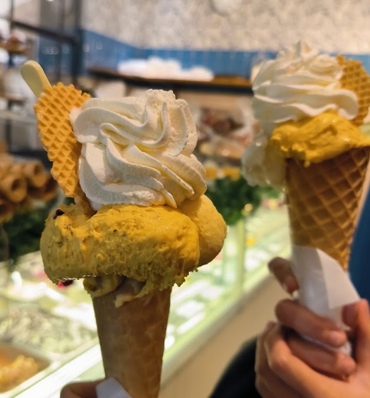 Due coni di gelato al pistacchio con panna montata, davanti al banco