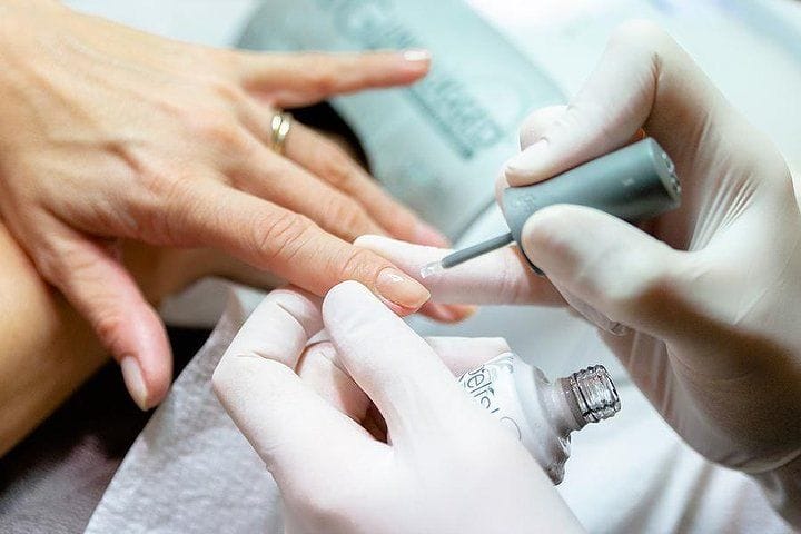 La manicure: le mani coi guanti stendono lo smalto chiaro.